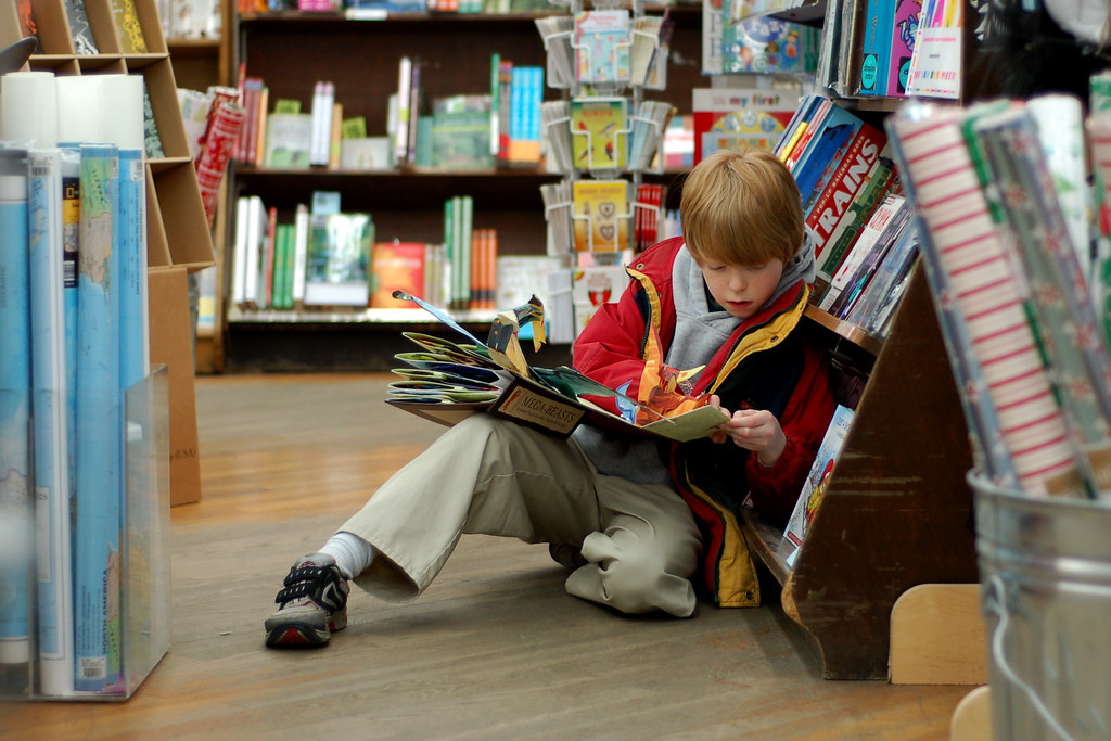 A child enjoys the magic of reading while in a local library. Child reading at Brookline Booksmith by GPA Photo Archive is licensed under CC BY-SA 2.0 DEED.